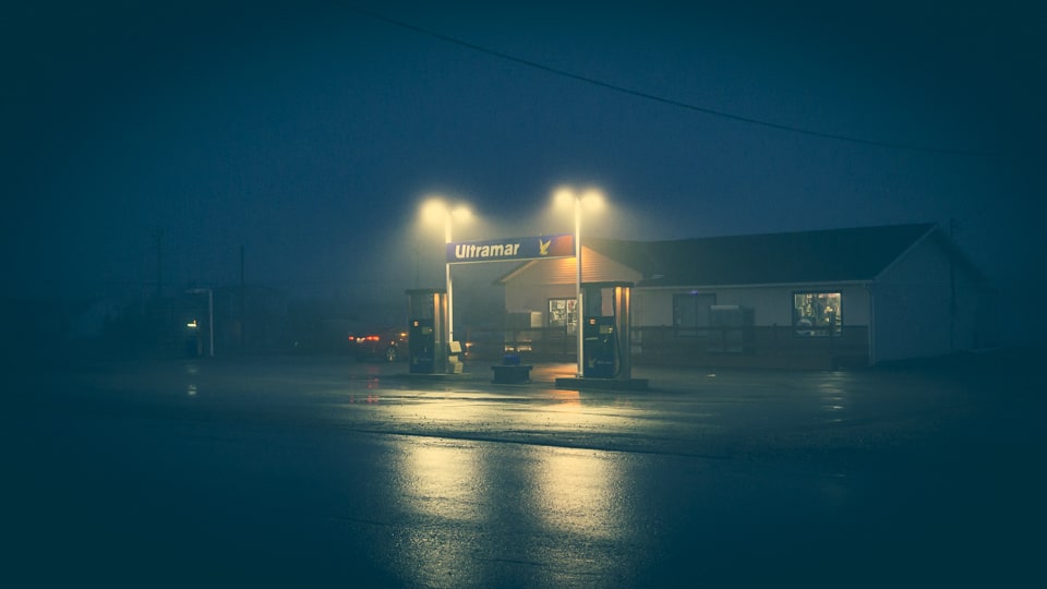 The misty night is only pierced by some streetlamps and gas station lights